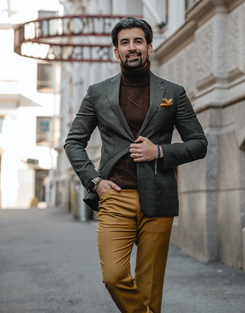 Close-up of a smiling man in a plaid suit with a boutonniere, outdoors.